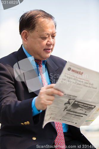 Image of Senior businessman in suit reading newspaper