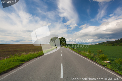 Image of Empty road between summer field at sunset