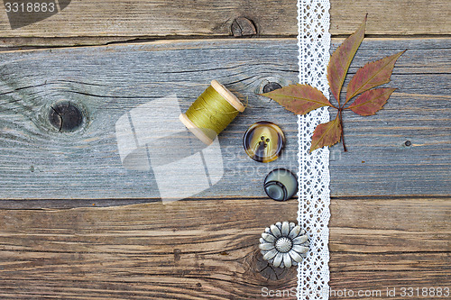 Image of lace ribbon, vintage buttons, spools of thread and dry leaves