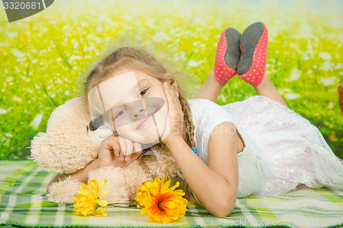 Image of Five-year girl hugging a teddy bear lying on picnic rug
