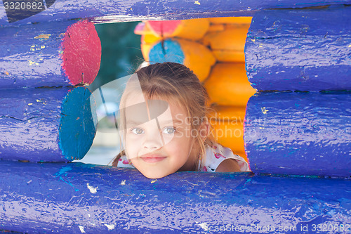 Image of Five-year girl looks out from a wooden window