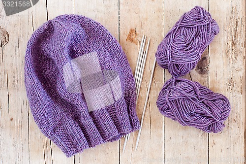 Image of wool purple hat, knitting needles and yarn 