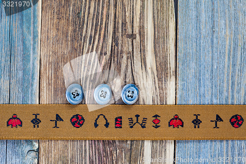 Image of aged tape with embroidered ornaments and three vintage buttons