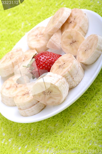 Image of Bunch of bananas and several strawberries on white plate