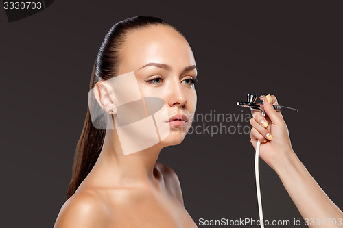 Image of visagist making makeup for model with aerograph