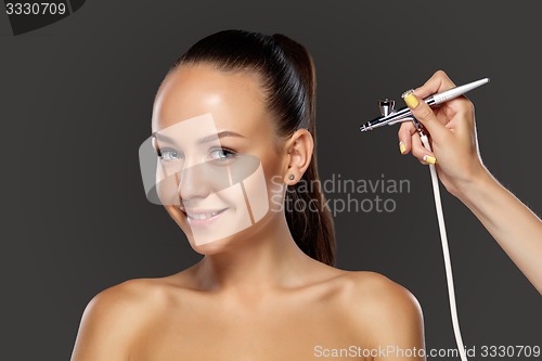 Image of visagist making makeup for model with aerograph