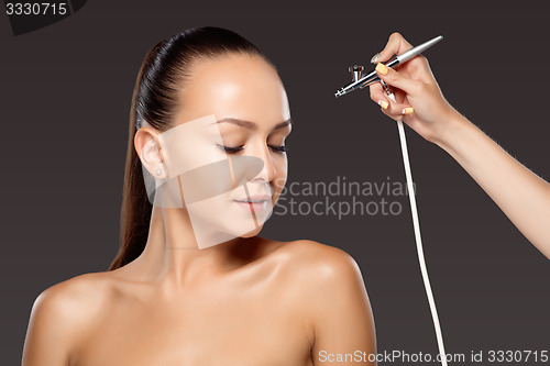 Image of visagist making makeup for model with aerograph