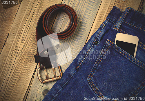 Image of old blue jeans, vintage leather belt and smartphone