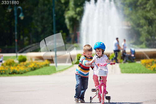 Image of Boy and girl in park learning to ride a bike