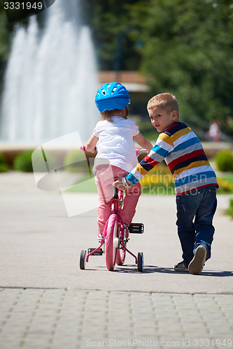 Image of Boy and girl in park learning to ride a bike