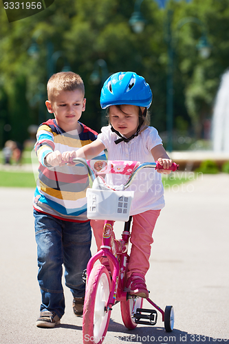 Image of Boy and girl in park learning to ride a bike