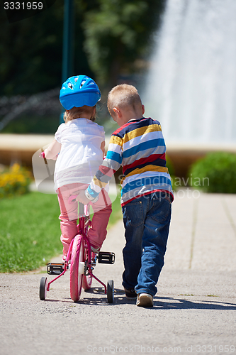 Image of Boy and girl in park learning to ride a bike