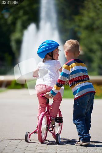 Image of Boy and girl in park learning to ride a bike