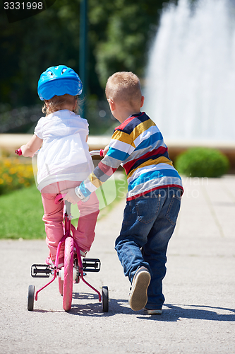 Image of Boy and girl in park learning to ride a bike