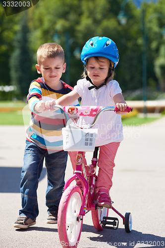 Image of Boy and girl in park learning to ride a bike
