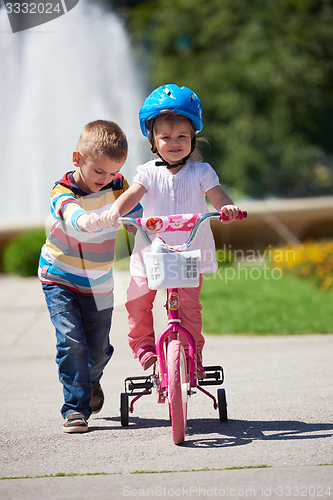 Image of Boy and girl in park learning to ride a bike
