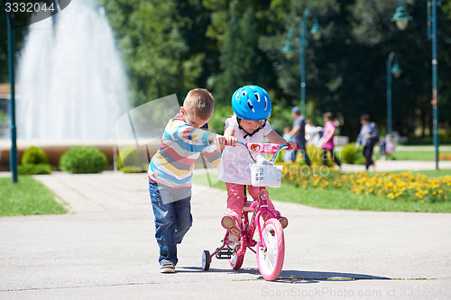 Image of Boy and girl in park learning to ride a bike