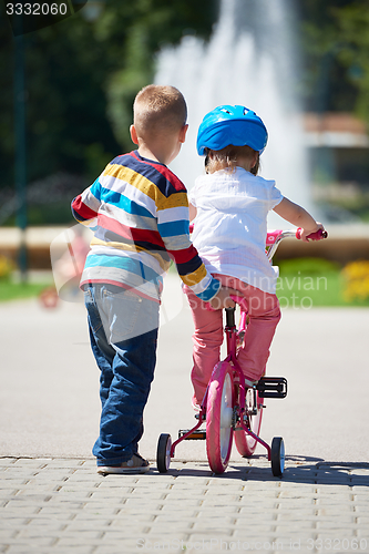 Image of Boy and girl in park learning to ride a bike