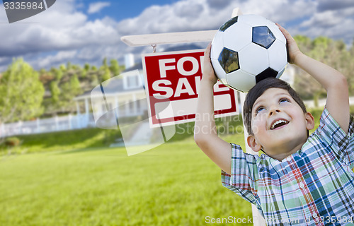 Image of Boy Holding Ball In Front of House and Sale Sign