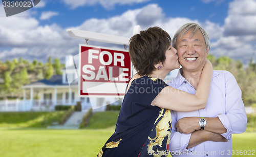 Image of Affectionate Senior Chinese Couple In Front of House and Sign