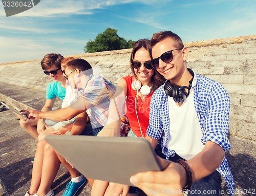 Image of group of smiling friends with tablet pc outdoors