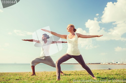 Image of smiling couple making yoga exercises outdoors