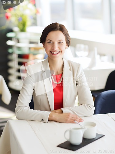 Image of happy woman sitting at table in restaurant