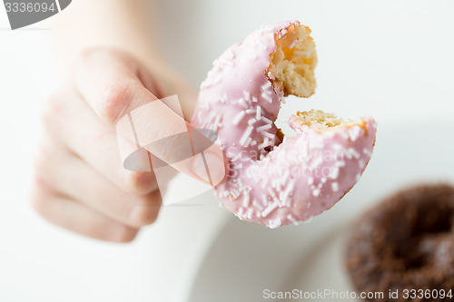 Image of close up of hand holding bitten glazed donut