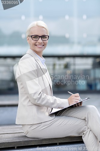 Image of young smiling businesswoman with notepad outdoors