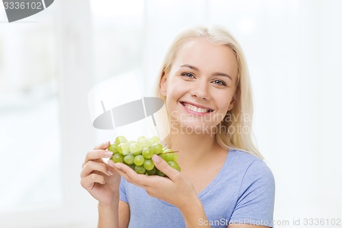 Image of happy woman eating grapes at home