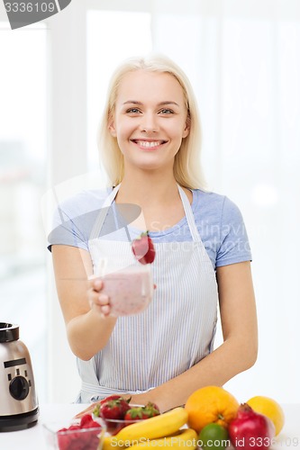 Image of smiling woman holding glass of fruit shake at home