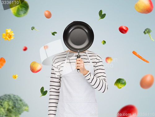 Image of man or cook in apron hiding face behind frying pan