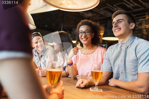 Image of happy friends drinking beer and talking at bar