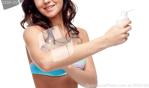 Image of happy young woman in swimsuit applying sunscreen