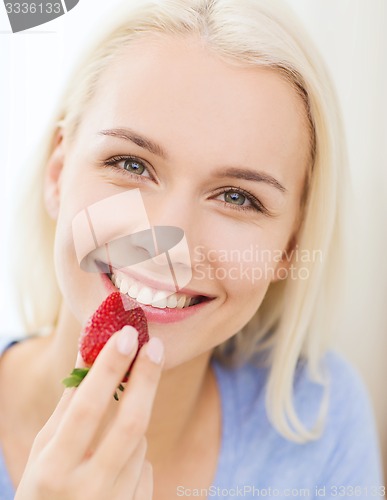 Image of happy woman eating strawberry at home