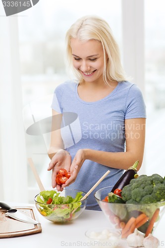 Image of smiling woman cooking vegetable salad at home