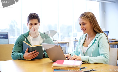 Image of happy students with laptop and books at library