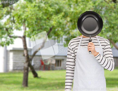 Image of man or cook in apron hiding face behind frying pan