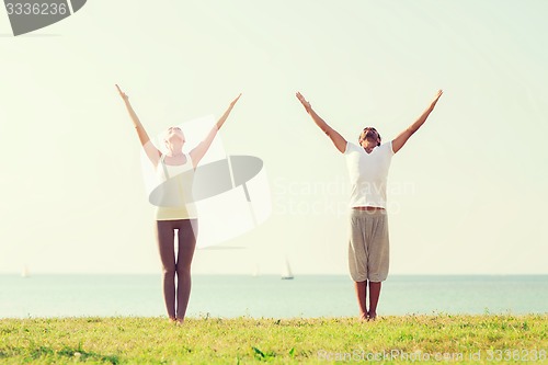 Image of smiling couple making yoga exercises outdoors