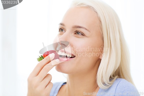 Image of happy woman eating strawberry at home