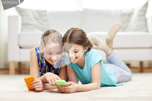 Image of happy girls with smartphones lying on floor