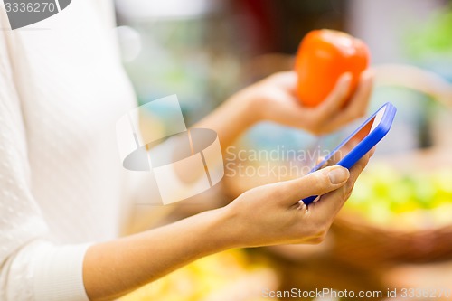 Image of woman with smartphone and persimmon in market