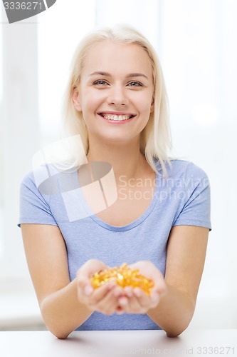 Image of happy woman holding fish oil capsules at home