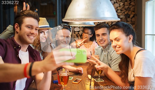 Image of happy friends with smartphone taking selfie at bar