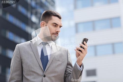 Image of serious businessman with smartphone outdoors