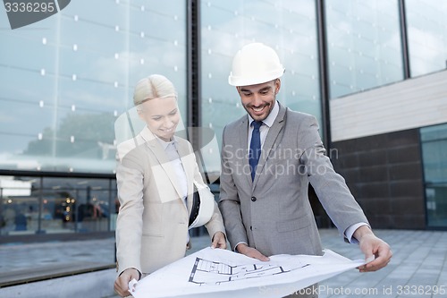 Image of smiling businessmen with blueprint and helmets