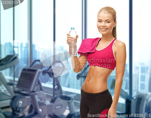 Image of happy woman with bottle of water and towel in gym