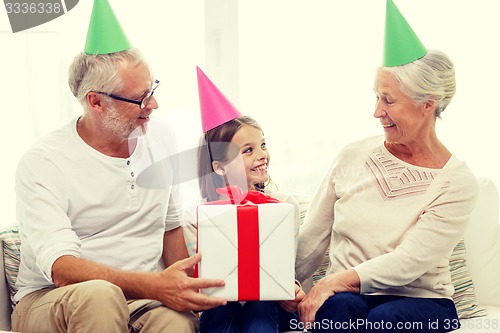 Image of smiling family in party hats with gift box at home