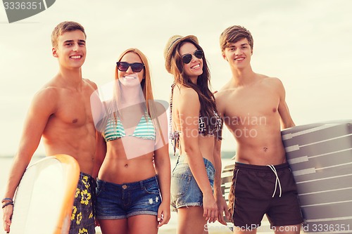 Image of smiling friends in sunglasses with surfs on beach