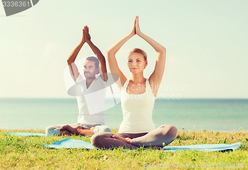 Image of smiling couple making yoga exercises outdoors